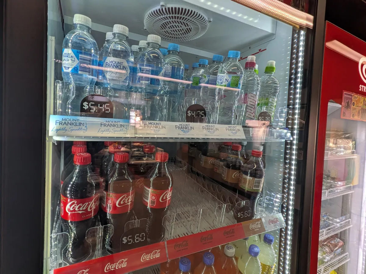 キャンパス売店の飲み物冷蔵庫。ミネラルウォーターに5.45豪ドルと4.75豪ドル、コカ・コーラに5.60豪ドルの値札が付いている
