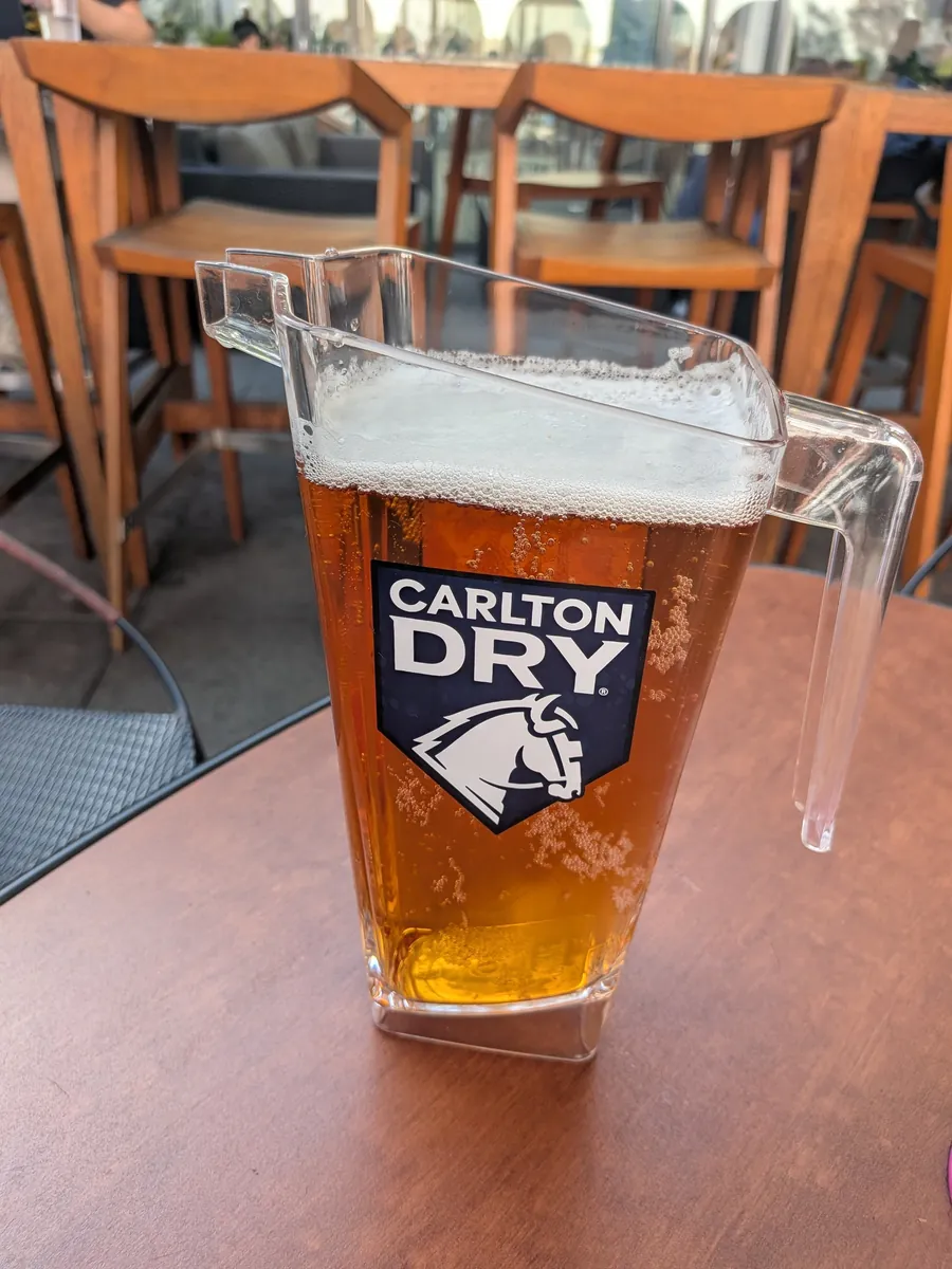 取っ手の付いた透明のジャグになみなみと注がれたカールトン・ドライのビール。木のテーブルに置かれている
