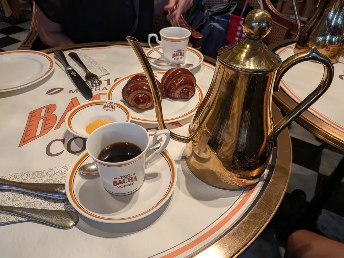 テーブルに置かれた金色のコーヒーポットとカップ、クロワッサン