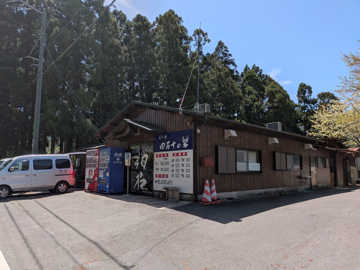 杉の木立に囲まれた木造の建物外観。駐車場には車が停まり、自動販売機や「四万十の碧」の看板が見える。