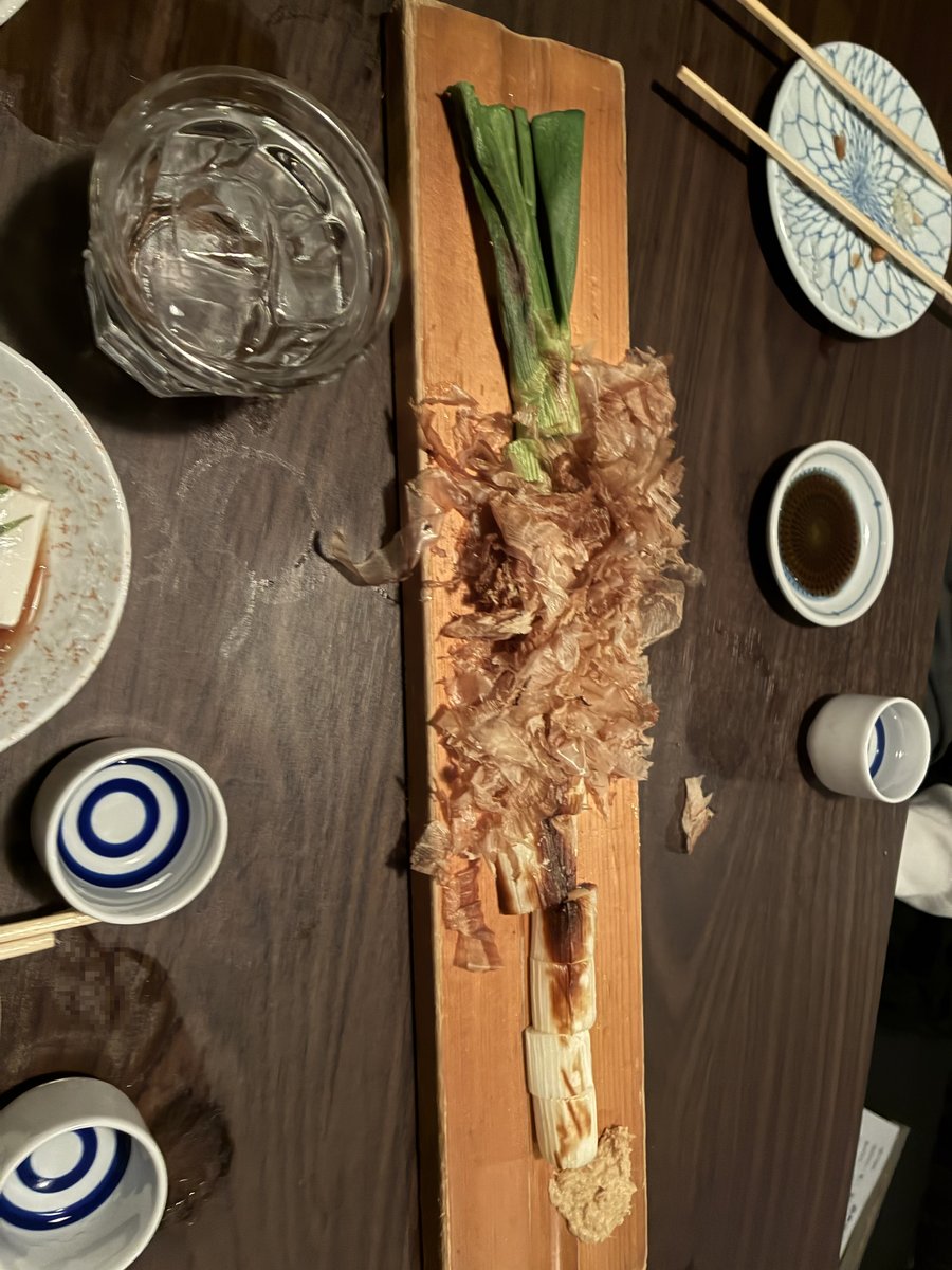 越後番屋酒場の焼きネギ。木の板の上に炙ったネギとかつお節が乗せられた、香ばしい一品。