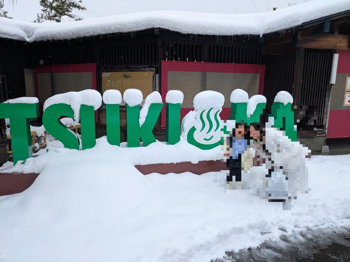 雪が積もった屋外で、「TSUKIKA」と書かれた緑色の大きなオブジェの前。中央には温泉マークがあしらわれ、楽しげな雰囲気が伝わる。