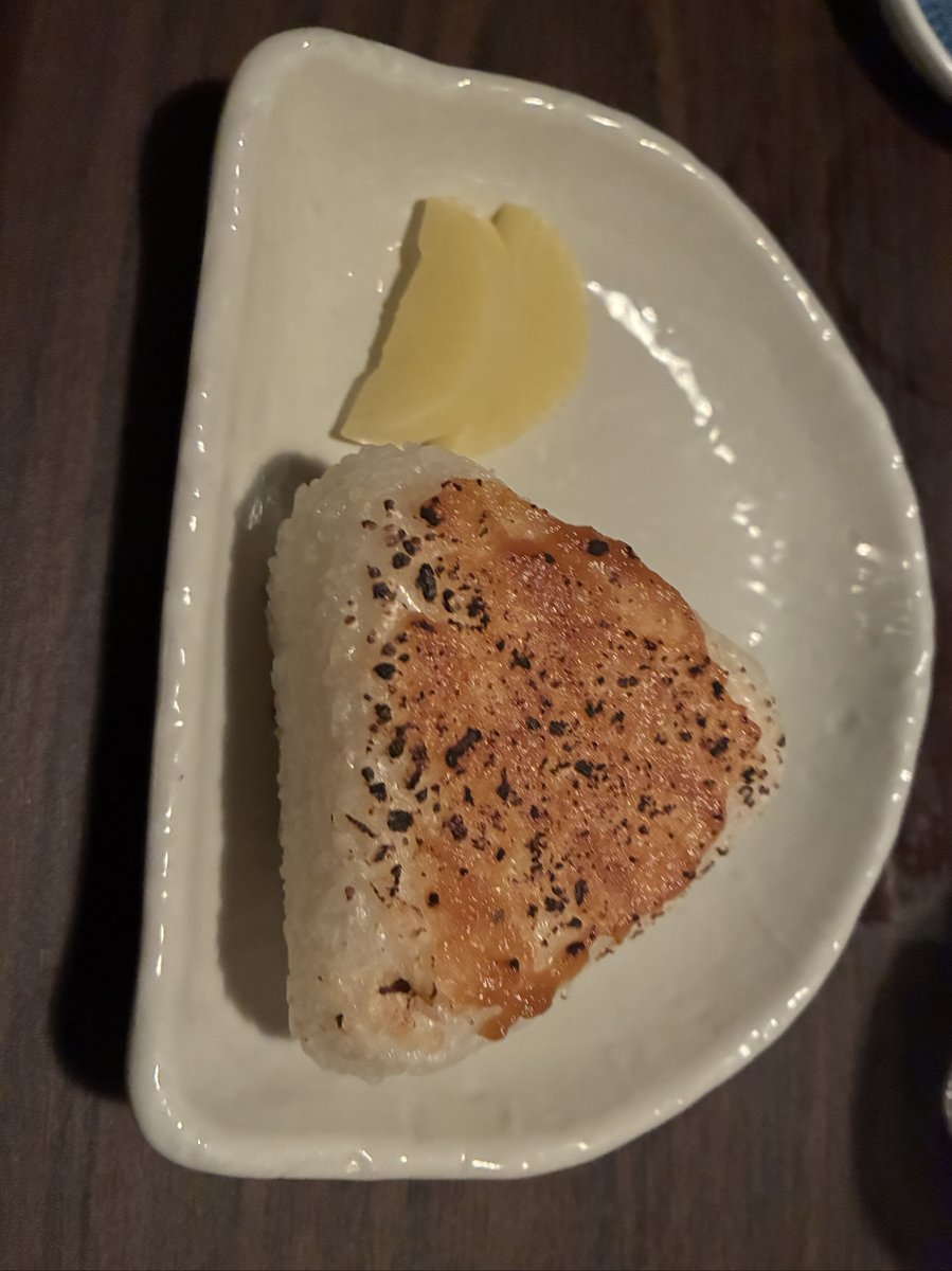 越後番屋酒場の焼きおにぎり。醤油が香ばしく焼けた三角おにぎりが白い皿に盛られ、ガリが添えられている。